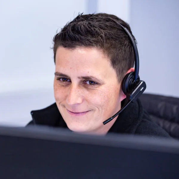 Eine bbt Mitarbeiterin mit Headset lächelt und schaut auf einen Bildschirm
